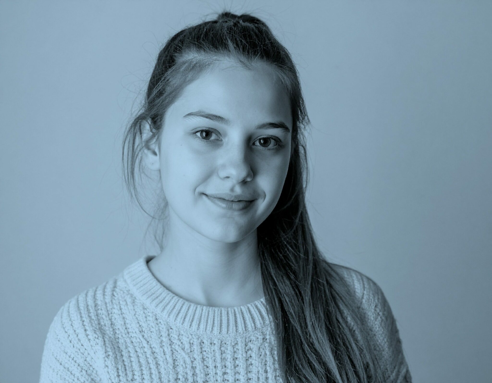 Portrait d’une jeune fille souriante en pull clair, sur fond uni bleu — image évoquant la jeunesse, la confiance en soi et l’exploration de l’avenir.